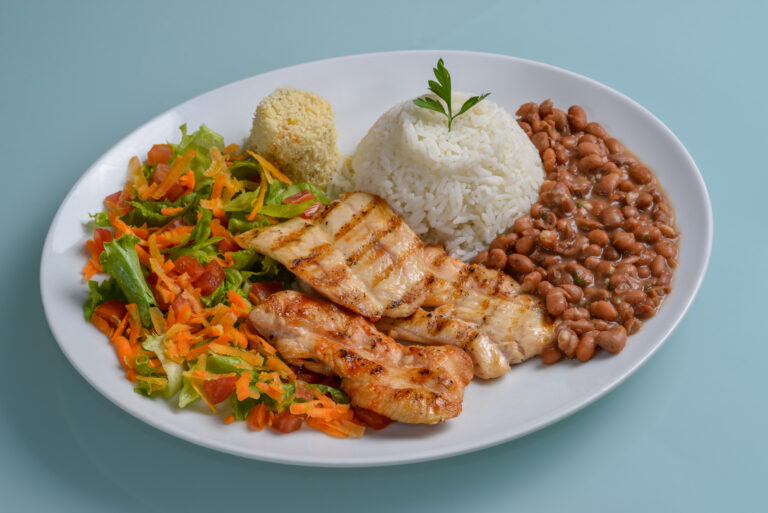 Brazilian healthy food. Plate with grilled chicken breast, accompanied by beans, rice, flour, vegetable salad in a white plate on the neutral table. Brazilian cuisine.